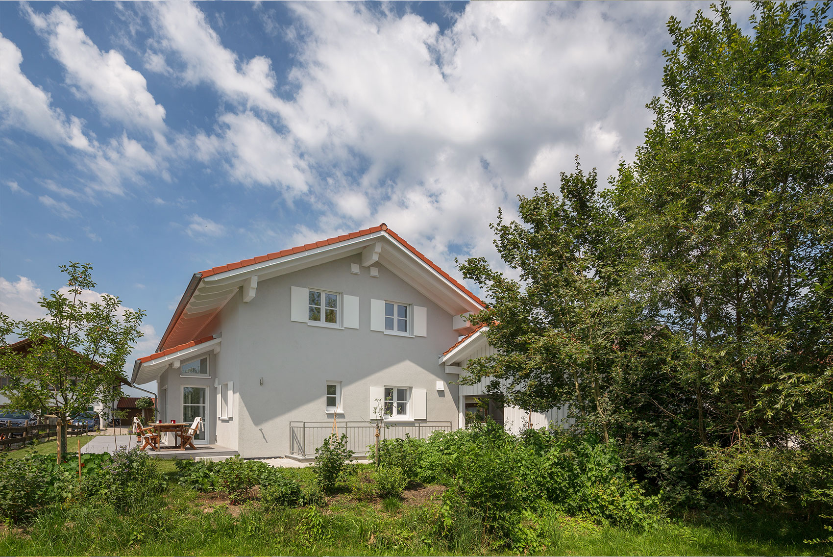 Giebelseite von Haus Ulmensee mit weißer Fassade zwischen Bäumen