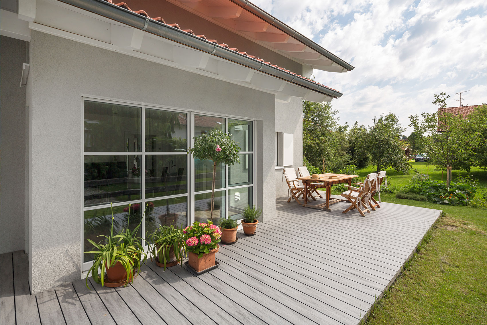 Holzterrasse von Haus Ulmensee mit Pflanzen und Gartenmöbeln vor großen Fenstern