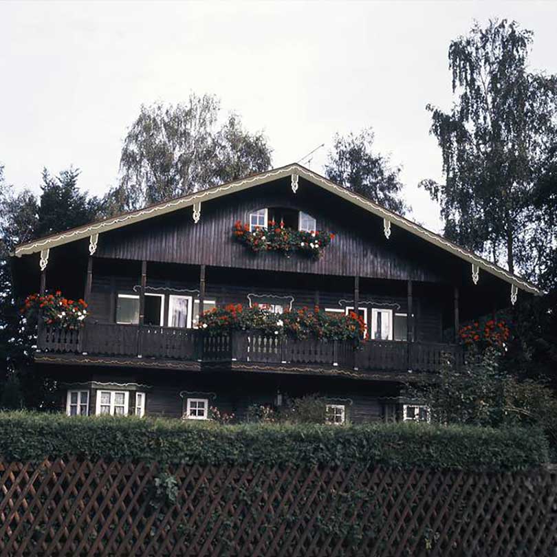 Historisches Isartaler Holzhaus · Archivaufnahme Historisches Isartaler Holzhaus mit Blumenschmuck an den Balkonen