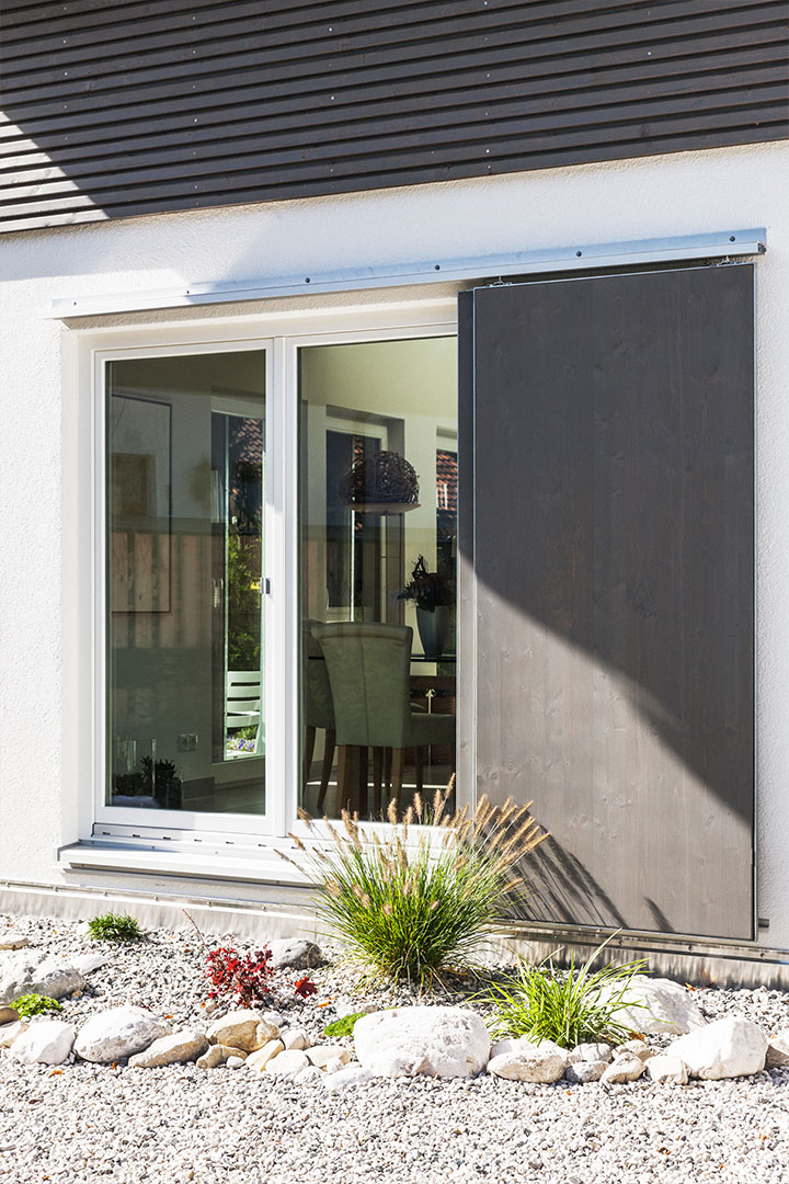 Großes Fenster mit dunklem Schiebeladen an einer hellen Hausfassade