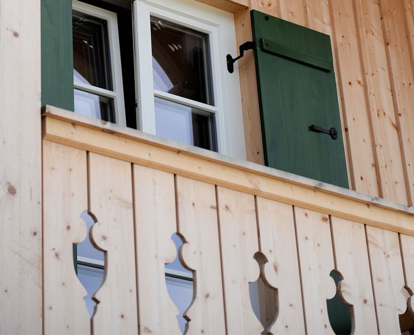 Fenster mit grünem Klappladen in einer hellen Holzfassade