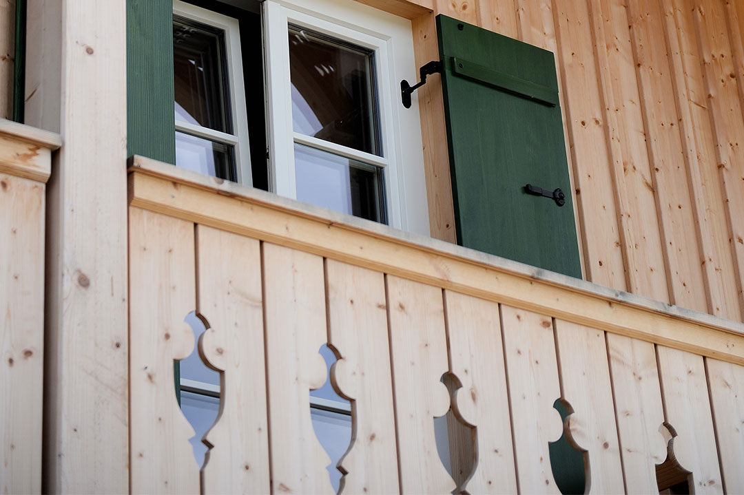 Fenster mit grünem Klappladen in einer hellen Holzfassade