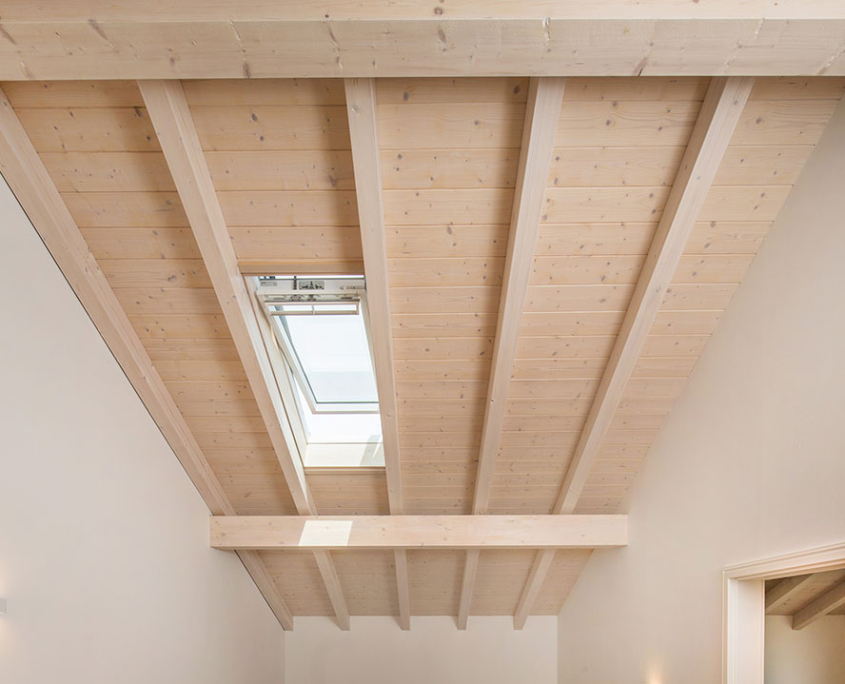 Dachfenster zwischen sichtbaren Holzbalken und heller Holzdecke