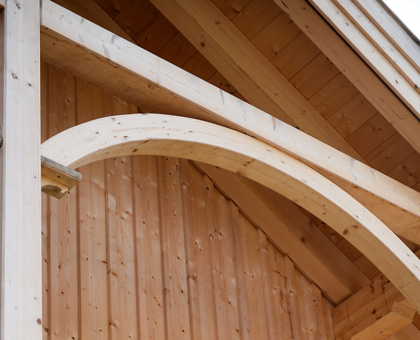 Geschwungener Holzbalken unter dem Dachüberstand eines Holzhauses mit Holzfassade