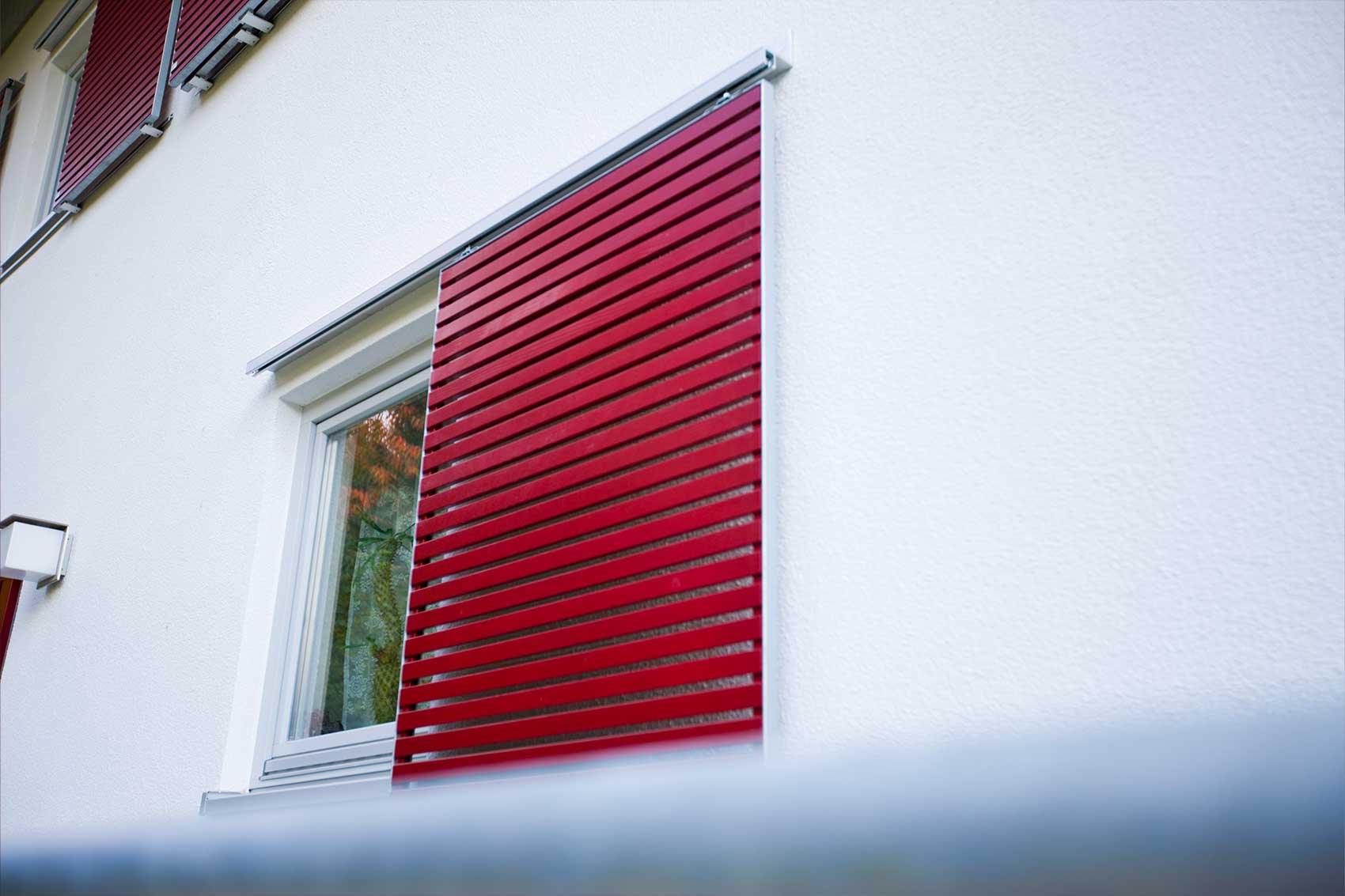 Roter Schiebelamellenladen an der hellen Putzfassade von Haus Langwiedersee