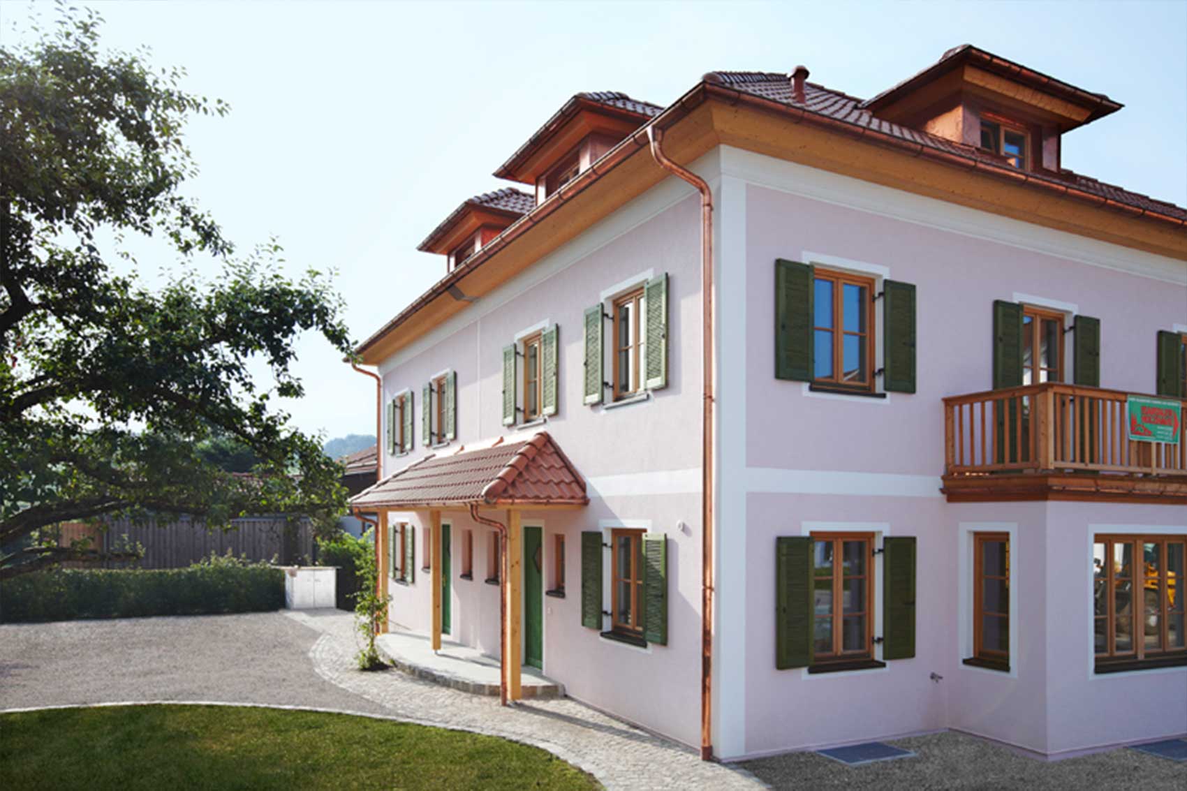 Haus Wörthersee · Seitenansicht Seitenansicht des Doppelhauses Wörthersee mit roten Dachziegeln und grünen Fensterläden