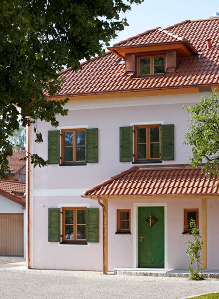 Fassade des Doppelhaus Wörthersee mit grünen Fensterläden und rotem Ziegeldach