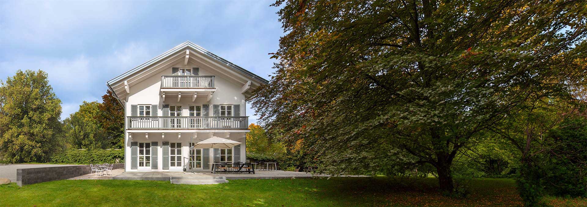 Holzfertighaus mit Balkonen · Slider Haus mit Satteldach und mehreren Balkonen, teilweise von einem Baum verdeckt