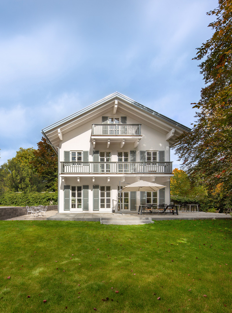 Haus mit Balkonen · Außenansicht Holzhaus mit Satteldach und mehreren Balkonen in einer Gartenanlage